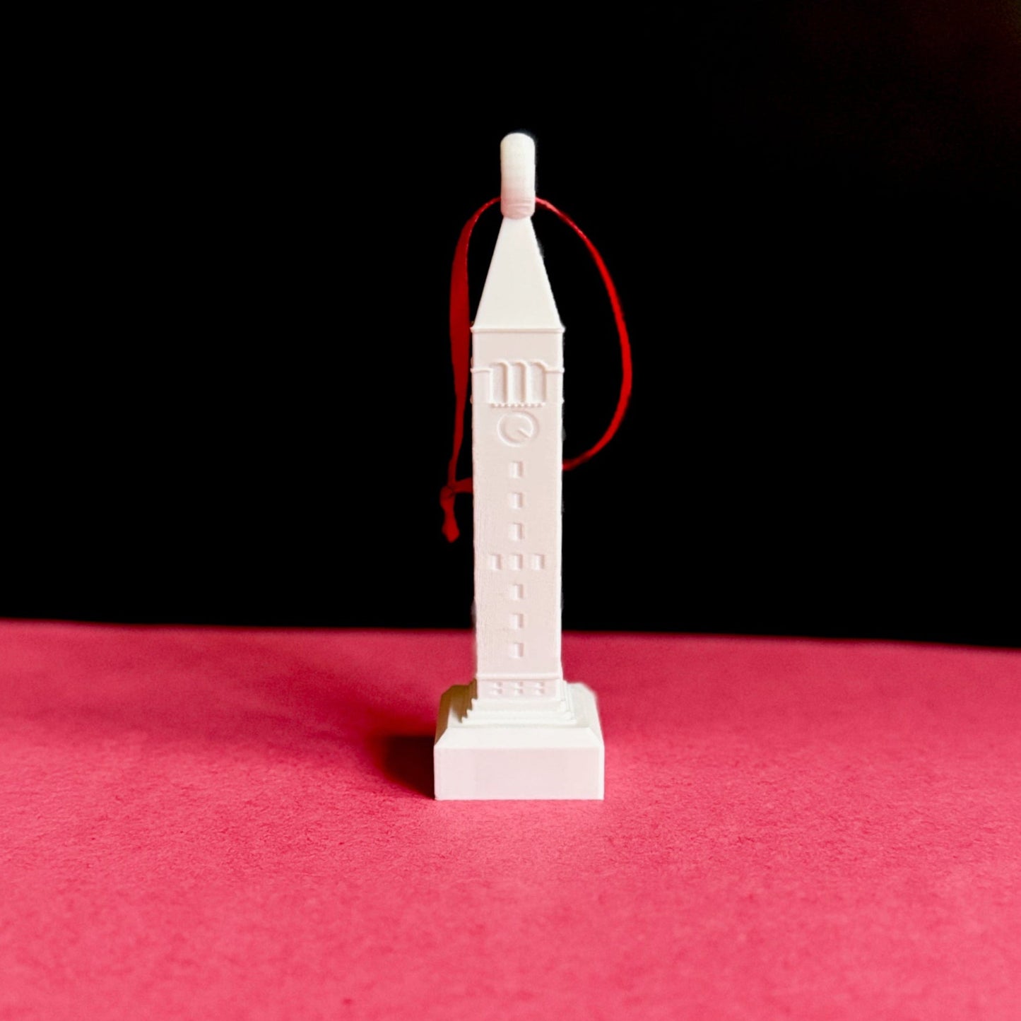 White 3D printed McGraw Tower ornament with red ribbon, perfect for holiday home dรฉcor.