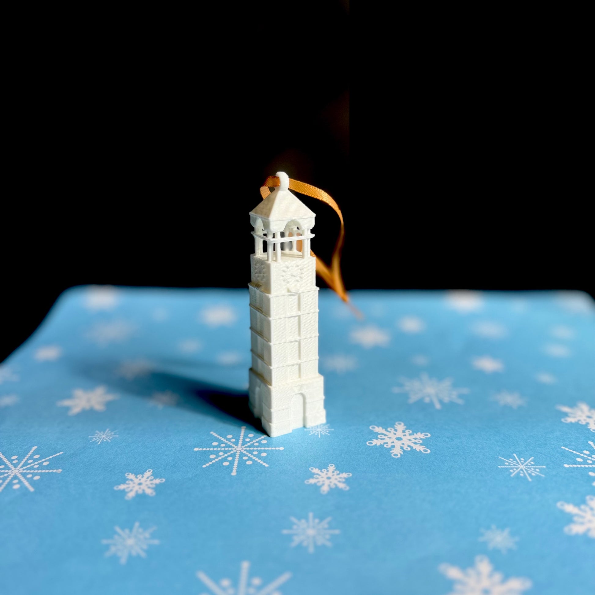 The Purdue Christmas ornament of the bell tower, shown on a blue holiday background. 