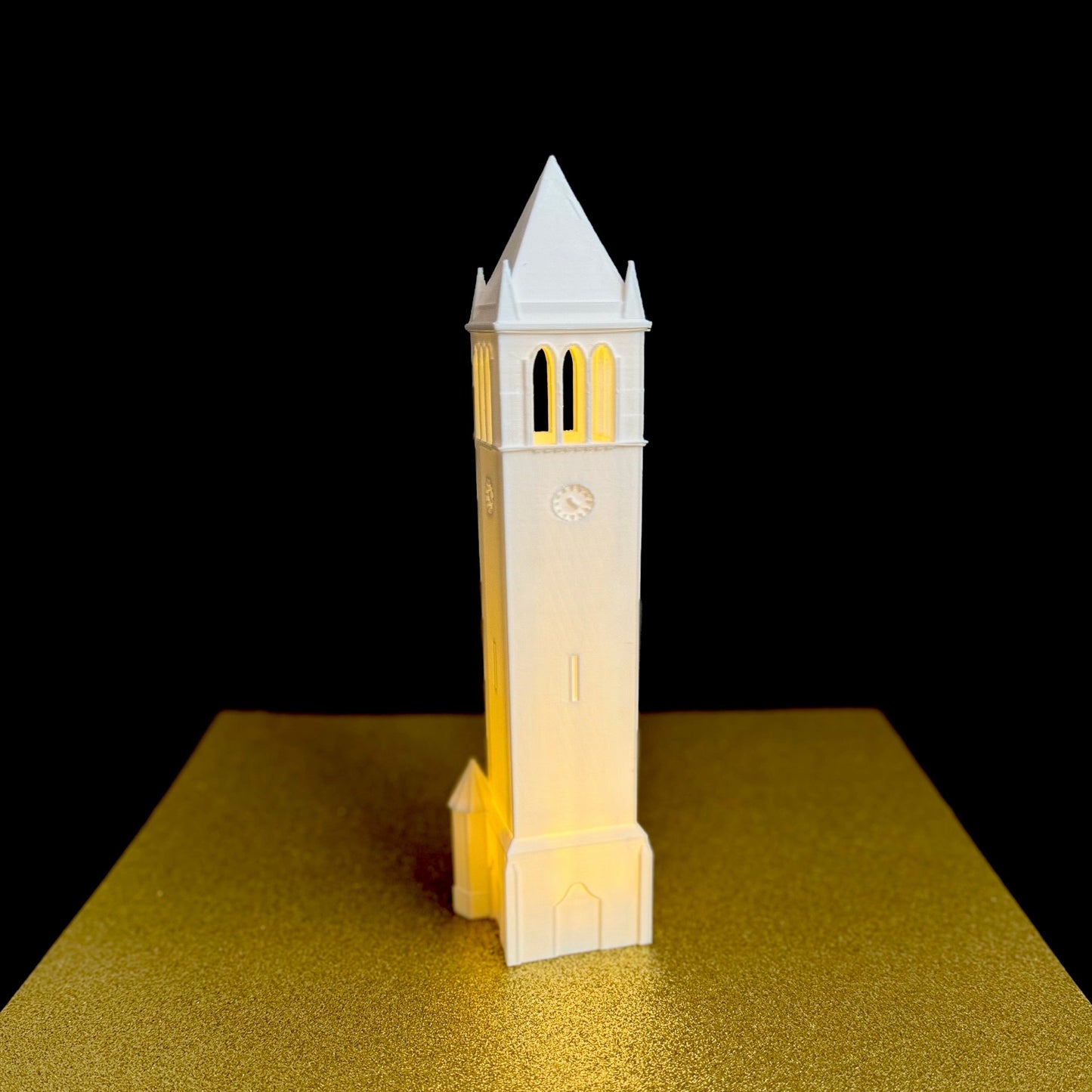 The Iowa State Campanile light, shown against a gold background.