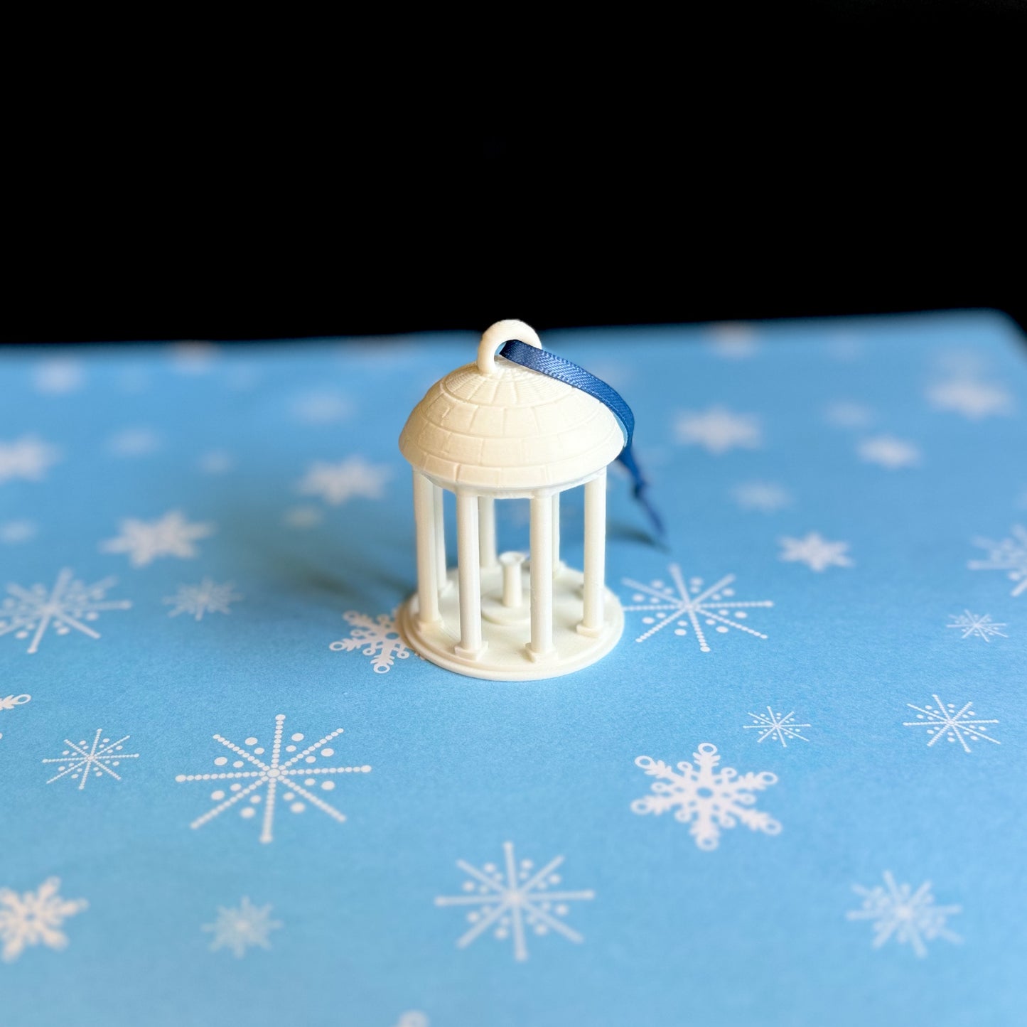 The UNC Old Well ornament, shown in detail against a blue holiday background.