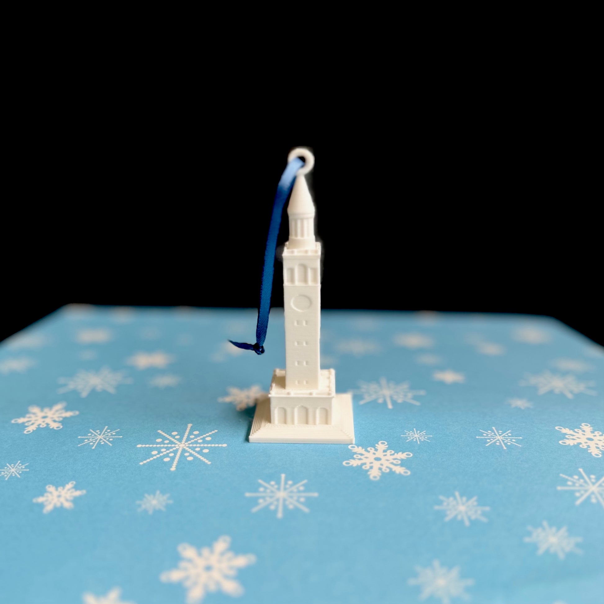 The UNC Bell Tower Christmas ornament, shown against a Carolina Blue background.