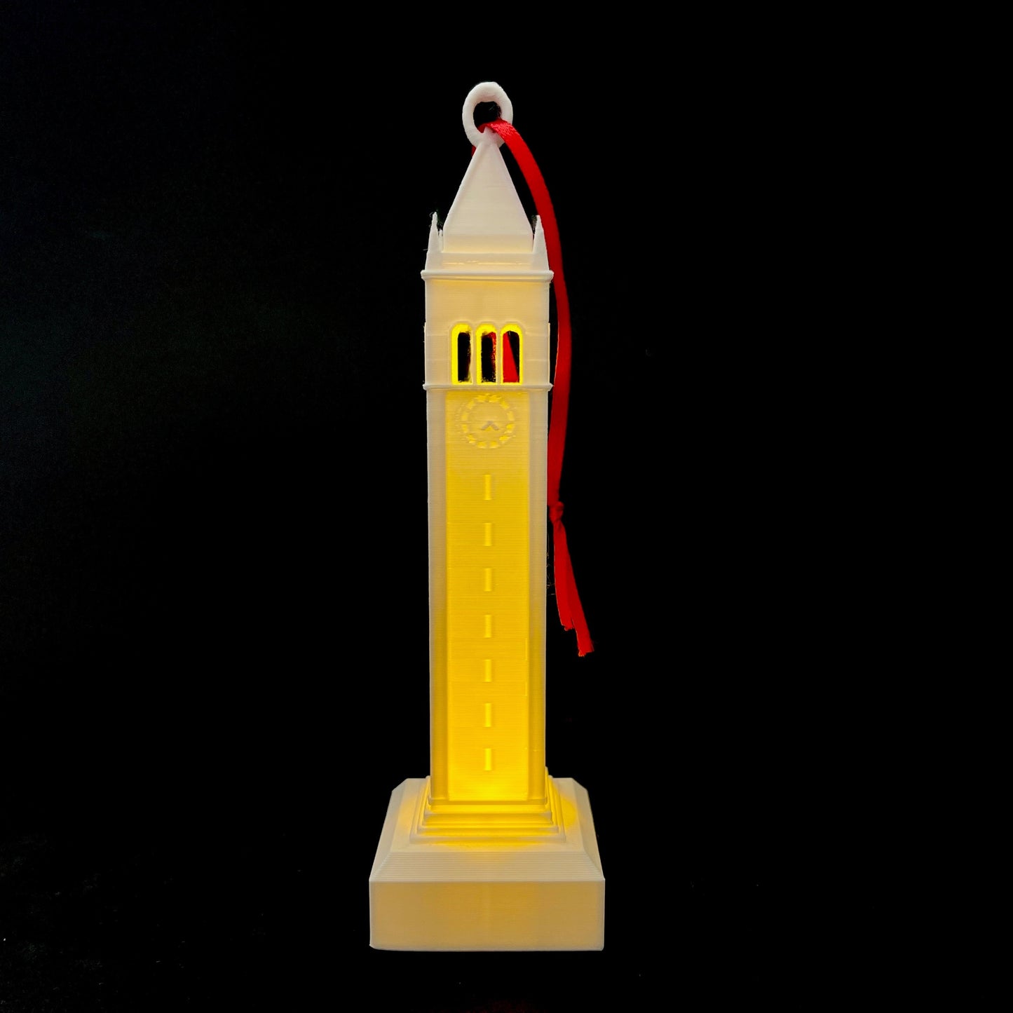 Front view of the Berkeley Sather Tower ornament with a light, shown against a black background.