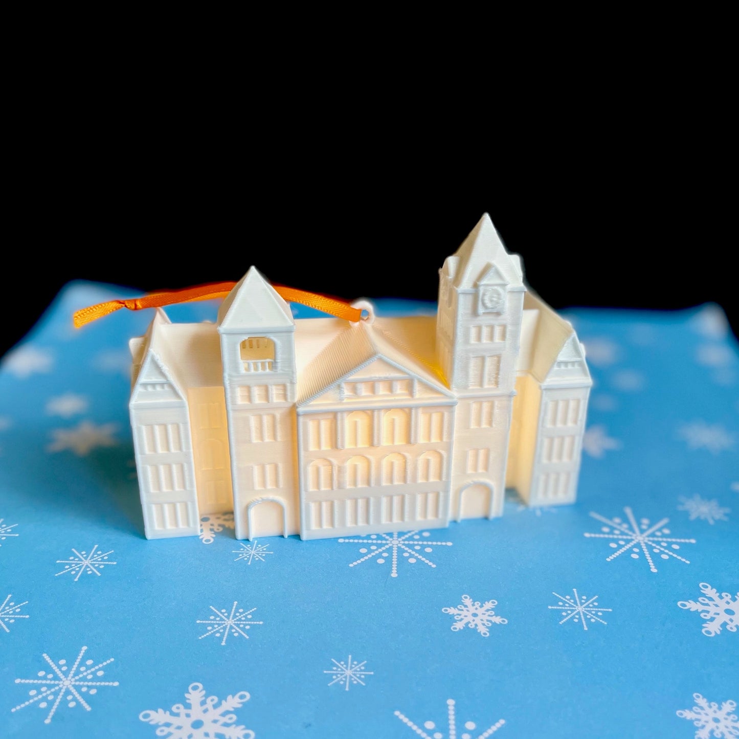 The lighted Auburn Samford Hall ornament, shown against a blue holiday background.