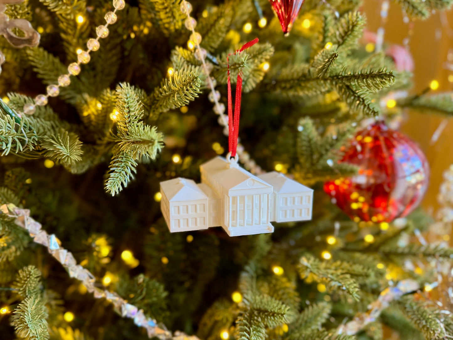Decorative ornament shaped like the Ole Miss Lyceum building on a Christmas tree with lights and red ornaments.