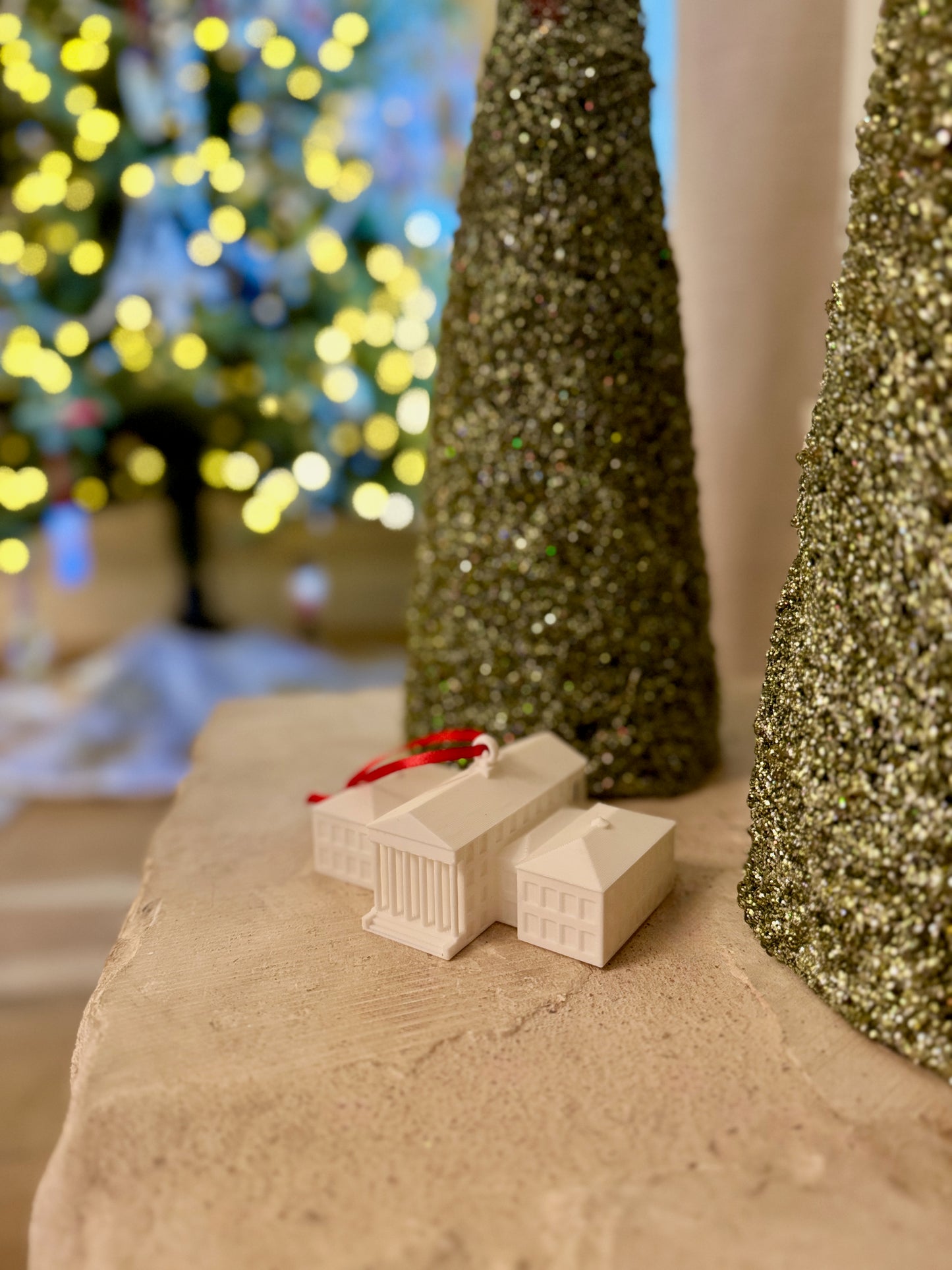 Small 3d printed Ole Miss ornament on a surface with decorative trees and lights in the background