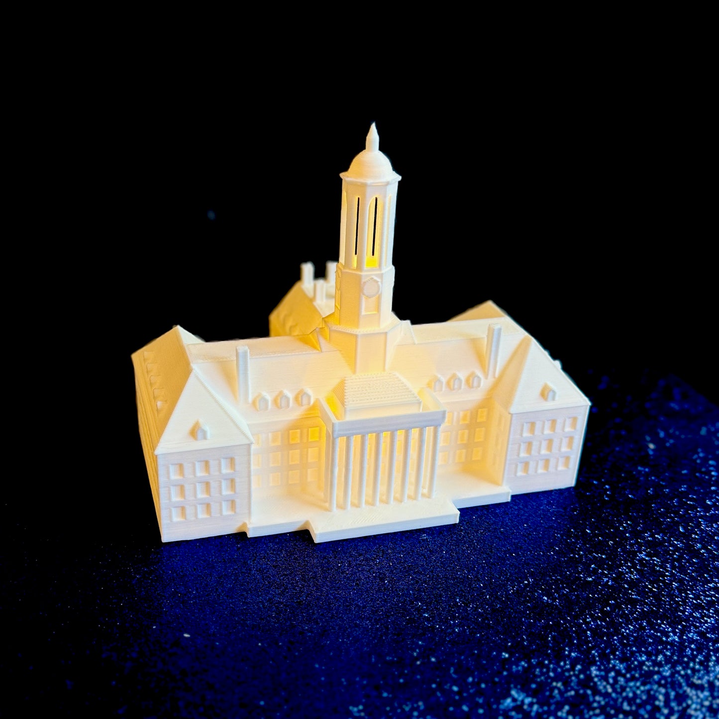 The lighted Penn State figurine of Old Main, shown against a blue background.