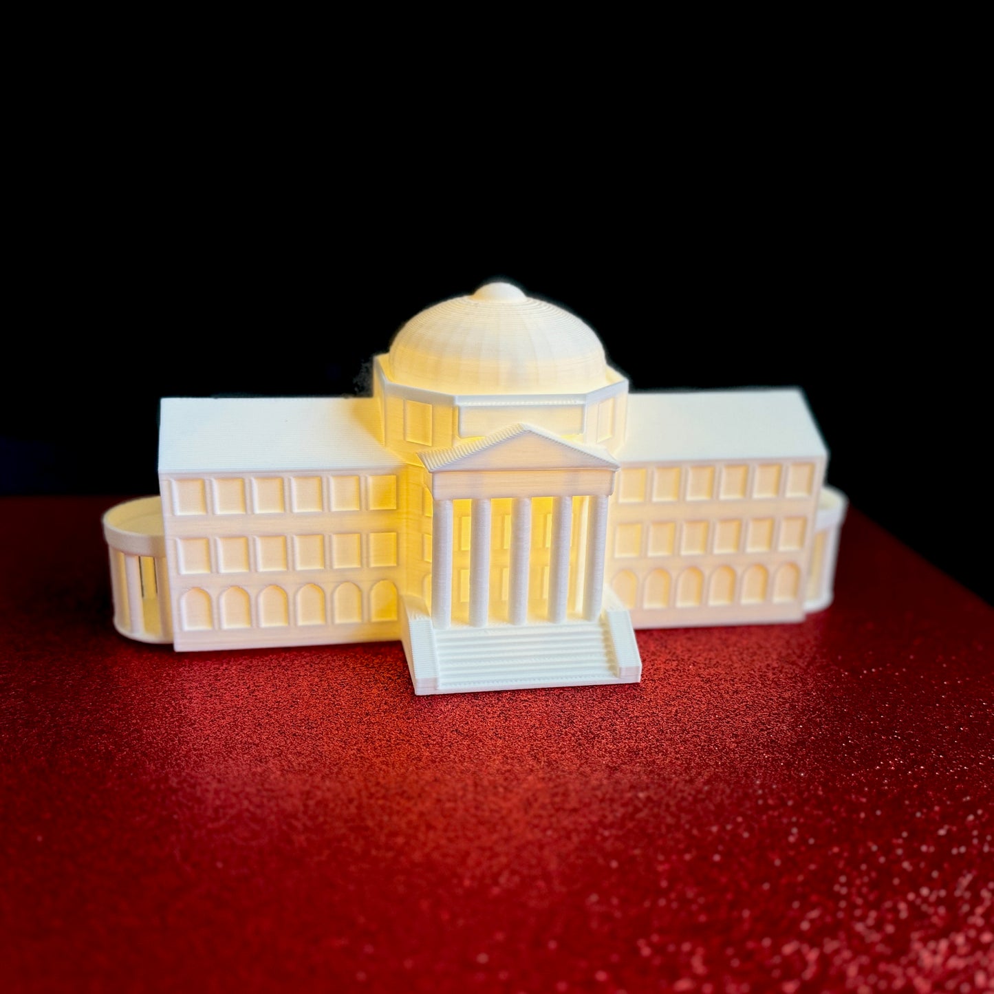 The lighted SMU figurine of Dallas Hall,  shown against a red background.