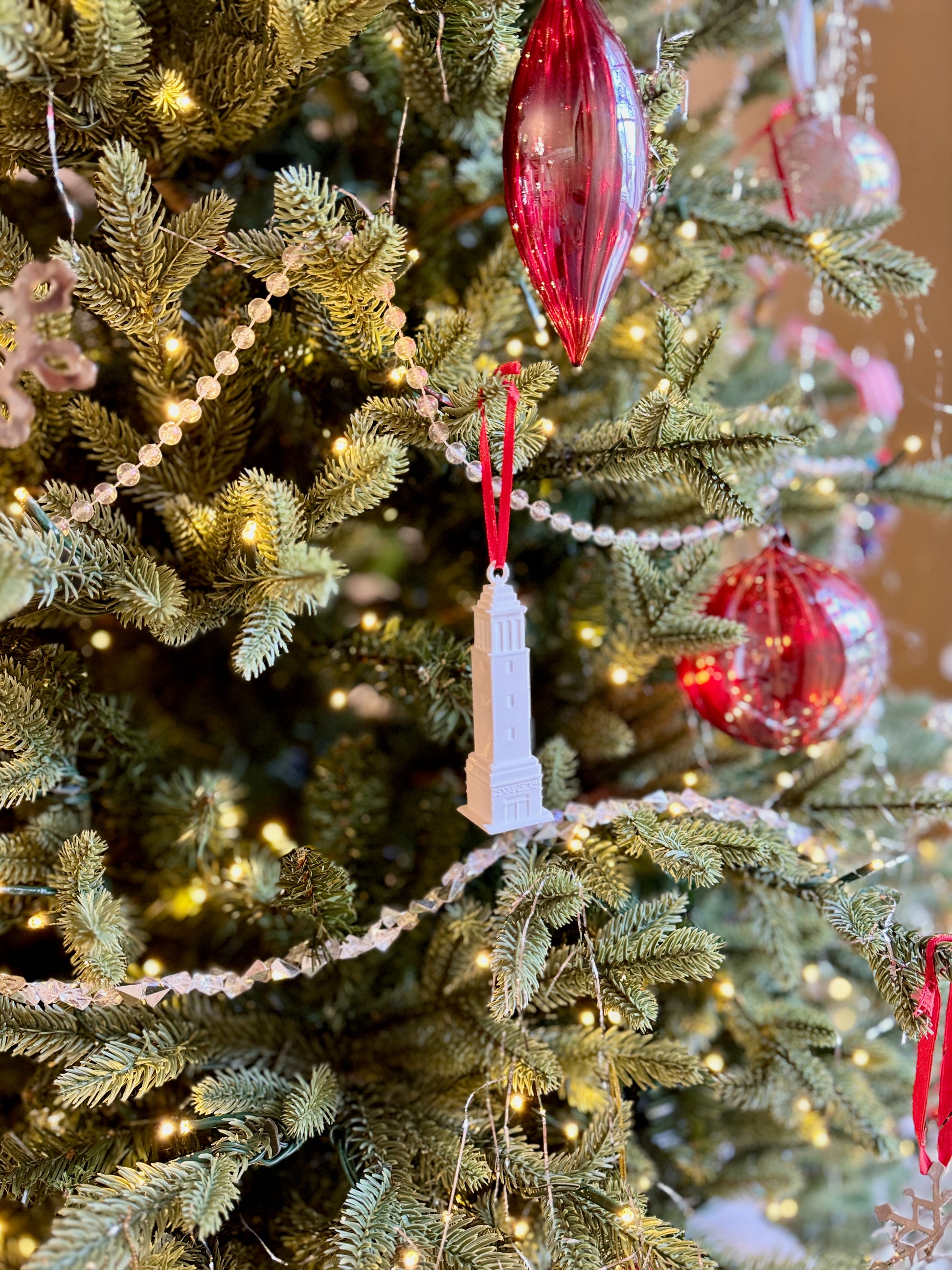 The Denny Chimes ornament for University of Alabama alumni, shown on a decorative Christmas tree with ornaments and lights