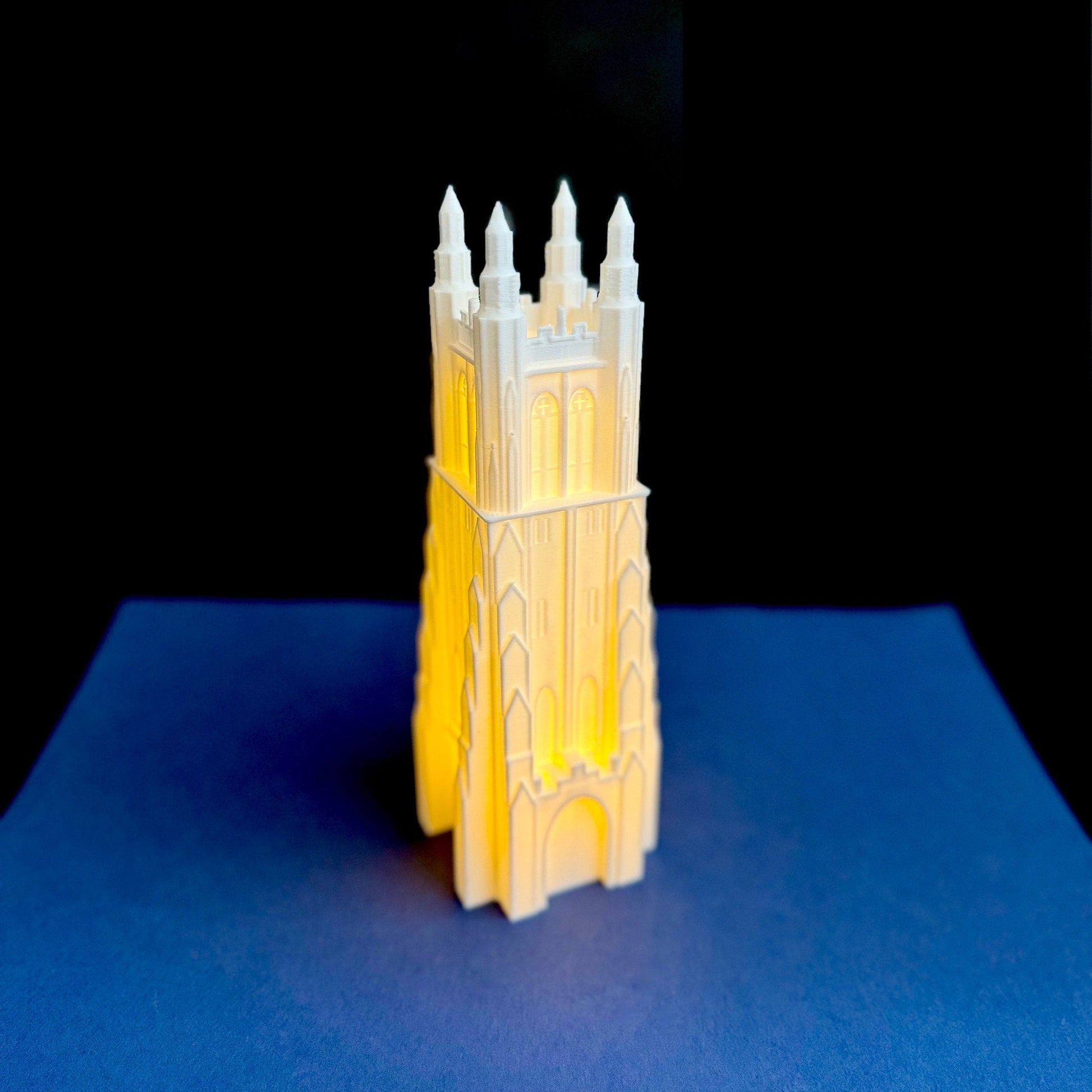 The lighted Duke Chapel figurine, shown against a blue background.