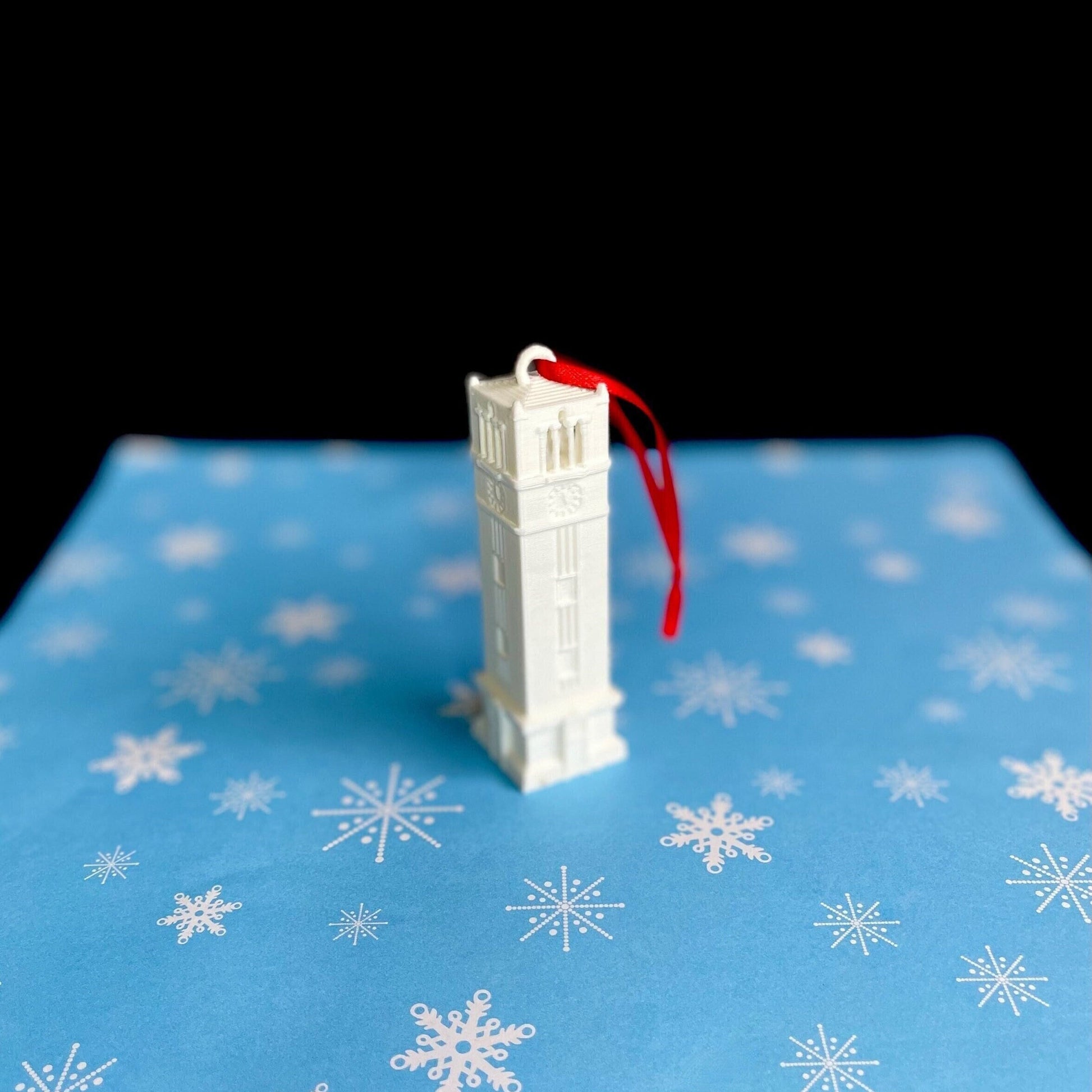 The NC State Christmas ornament, displayed against a blue holiday background.