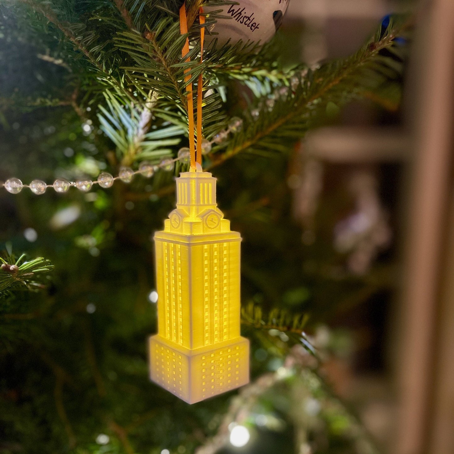 Front view of the lighted UT Tower ornament, shown on a Christmas tree.