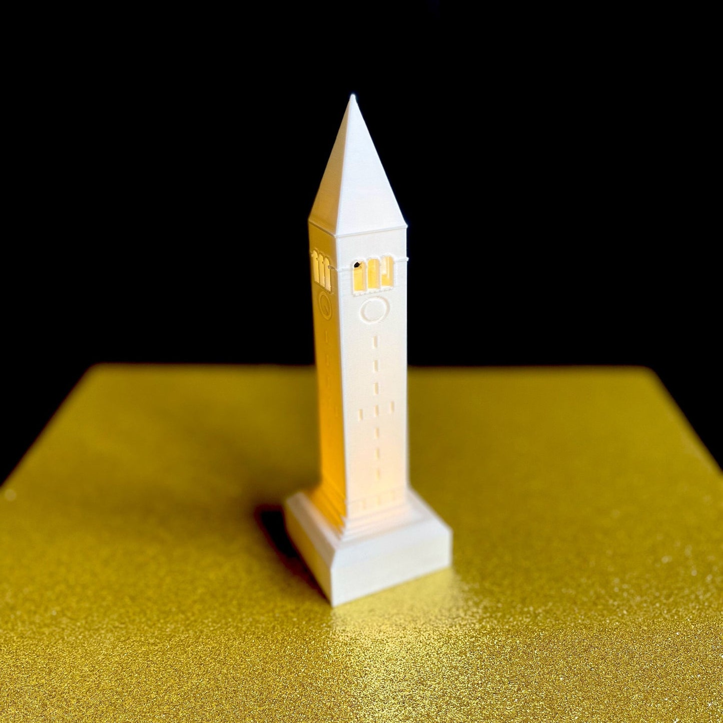 The lighted Cornell tower figurine, shown against a gold background.