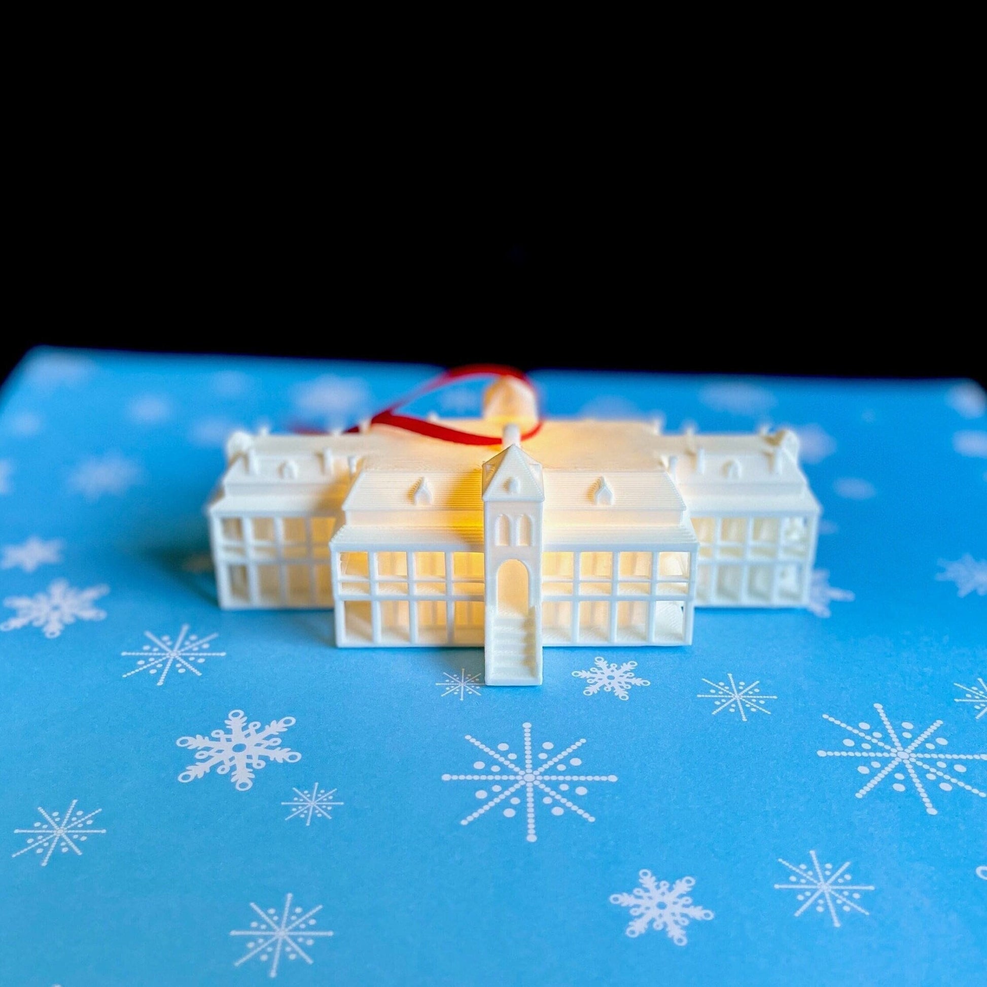 The lighted University of Arizona Old Main ornament, shown on a blue holiday background.